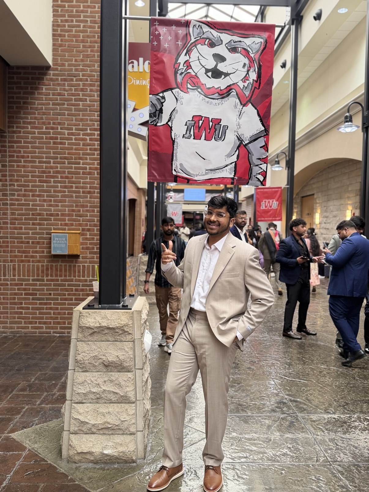 Bharath Chandra standing beneath an Indiana Wesleyan University banner on graduation day